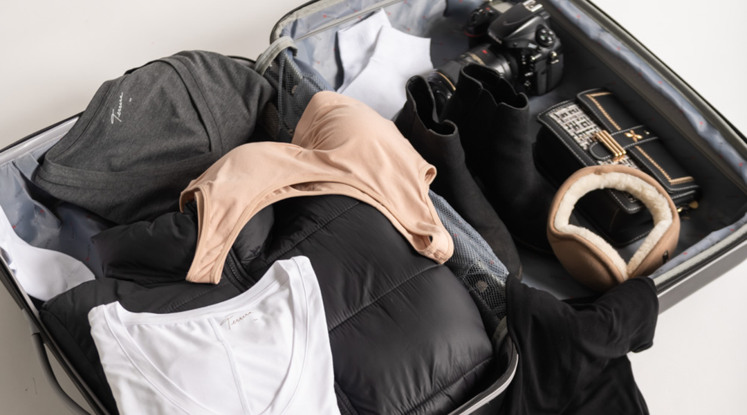 A packed suitcase with a bamboo bralette, Terrera bamboo long sleeve shirt, Aritzia Super Puff coat, earmuffs, and a camera. 