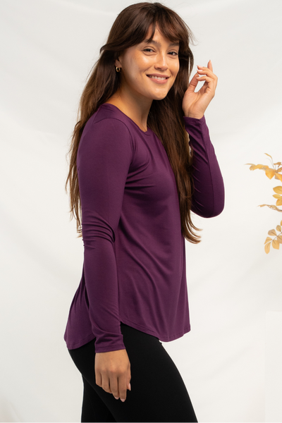 Woman wearing purple bamboo long sleeve top with curved hemline and crew neckline.