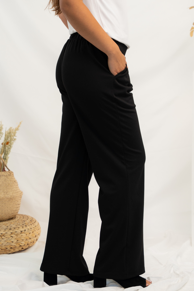 Side view of black pleated pants showing side pockets and wide legs.