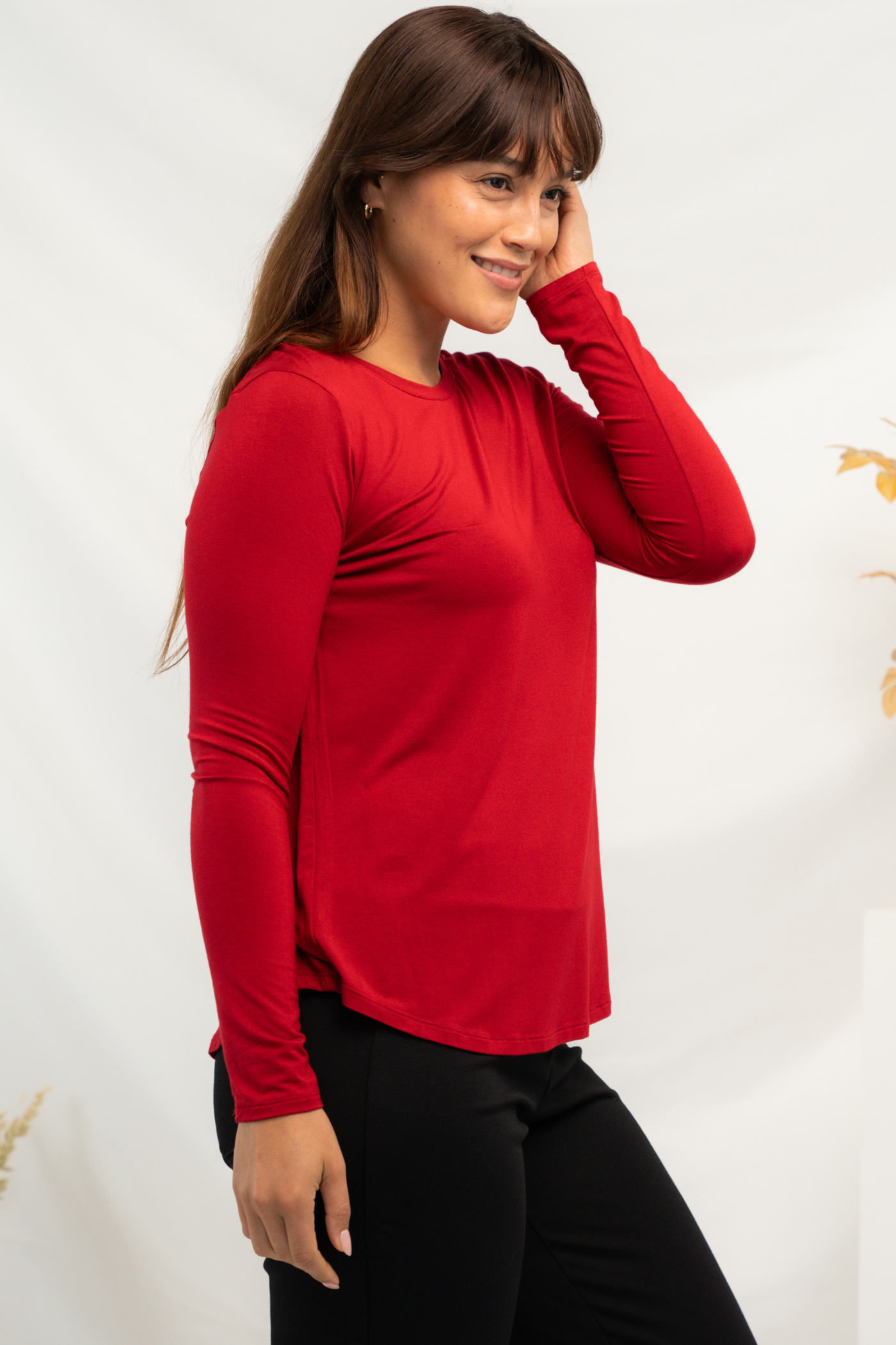 Side view of woman wearing a red long sleeve top with curved hemline. 