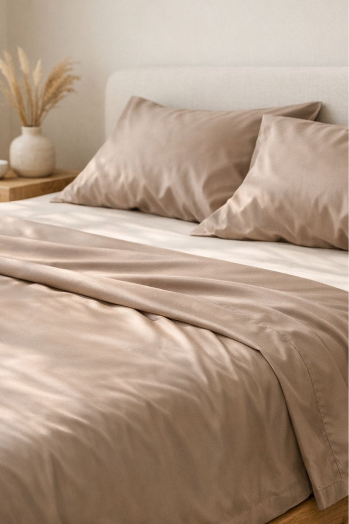 A cozy bed styled with a warm taupe bamboo sheet set in a bright, minimalist room with natural light.