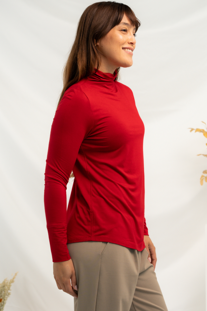 Side view of a red long sleeve top with funnel-neck and curved hemline.