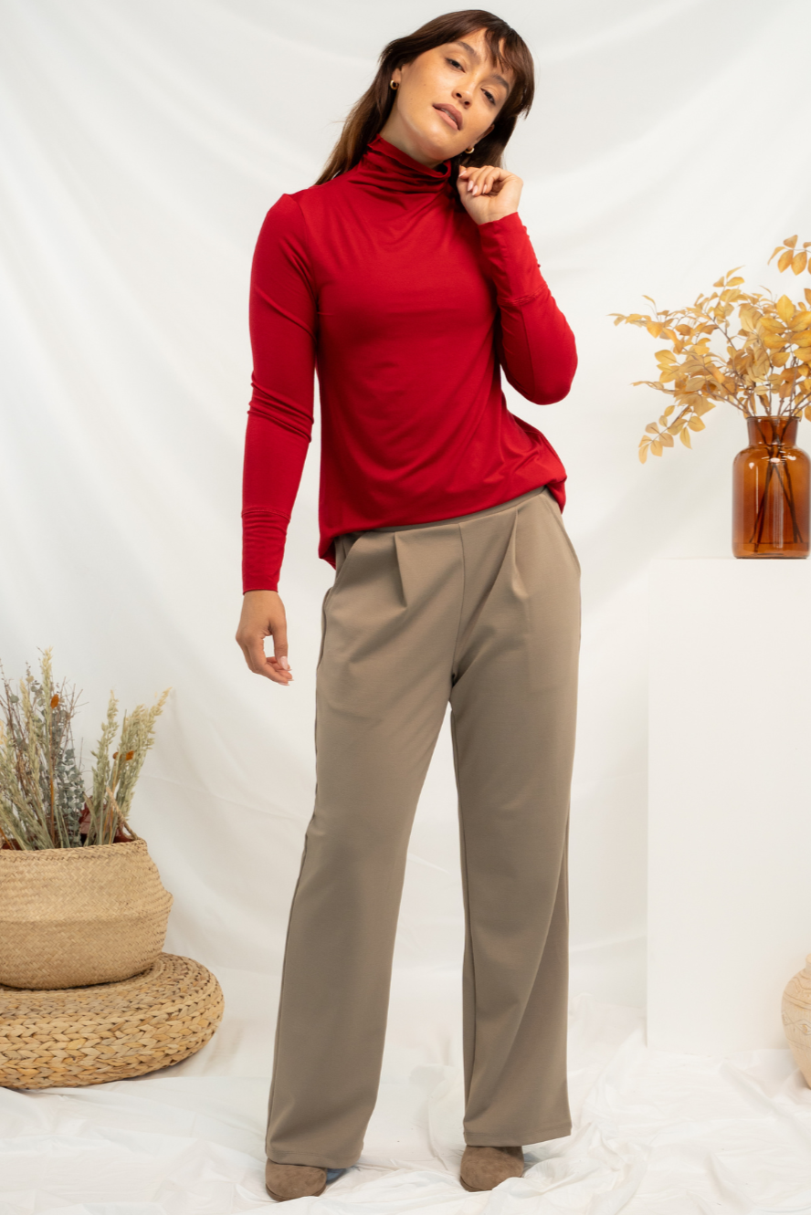 A woman wearing a red turtleneck long sleeve top half tucked into khaki pleated pants paired with brown flats.