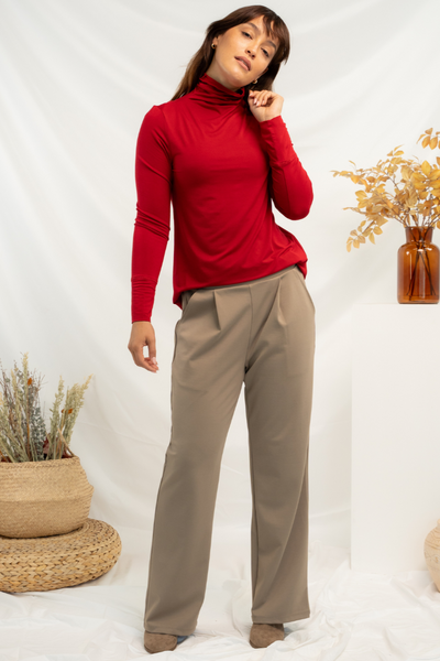 A woman wearing a red turtleneck long sleeve top half tucked into khaki pleated pants paired with brown flats.