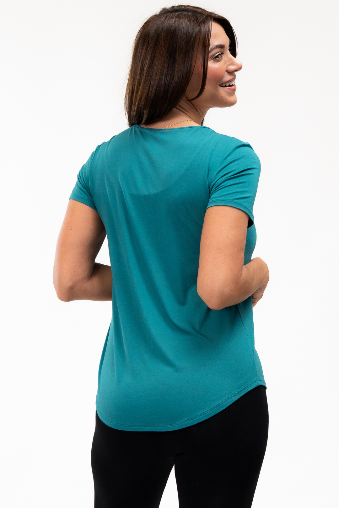 Woman wearing a teal t-shirt on a white background showing the lower back hem for extra coverage