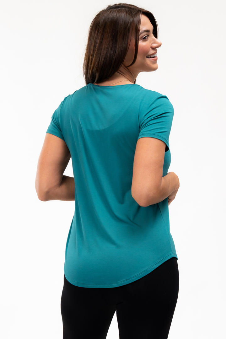 Woman wearing a teal t-shirt on a white background showing the lower back hem for extra coverage