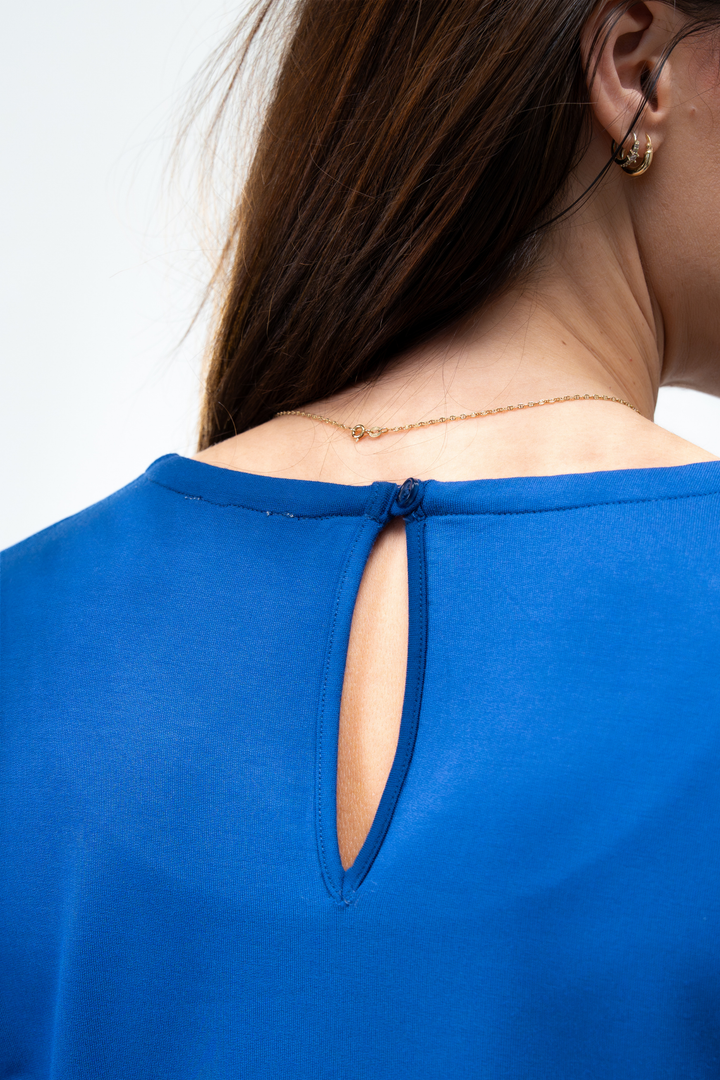 A blue top with a cut-out design on the back, with small button closure