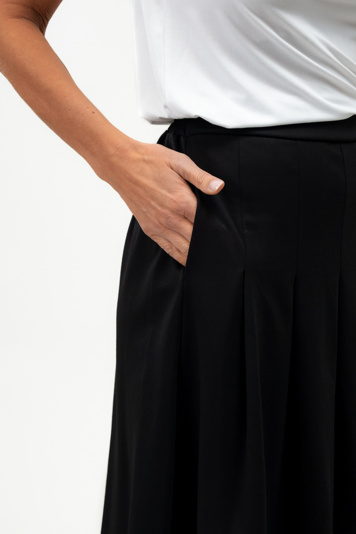 Person wearing a white top and black pants with one hand in the pocket on a light gray background