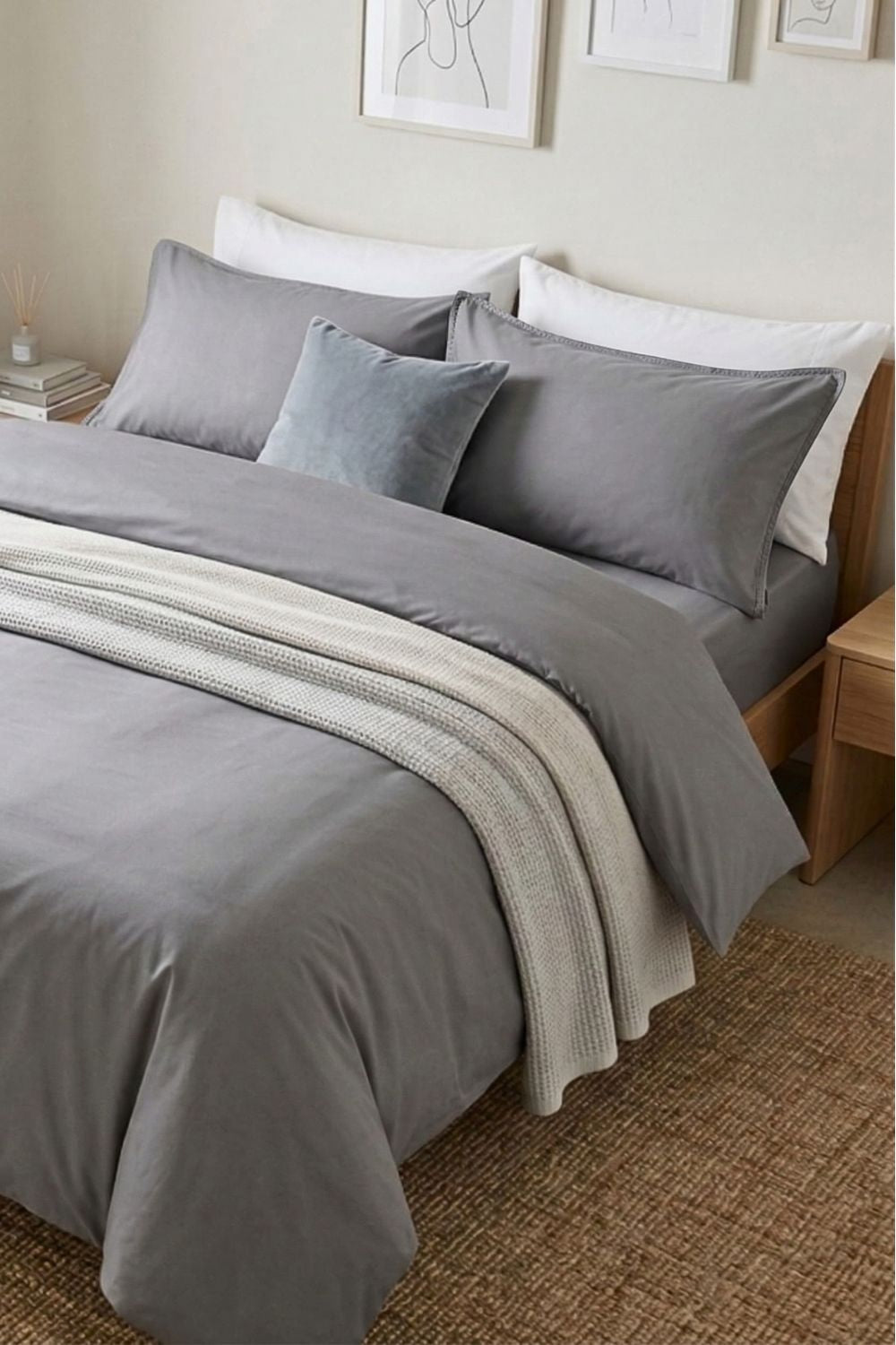 A bright and airy bedroom featuring a light grey duvet cover. The bedding is styled with cozy neutral pillows and throws, creating a versatile and calming atmosphere in a modern sustainable home.