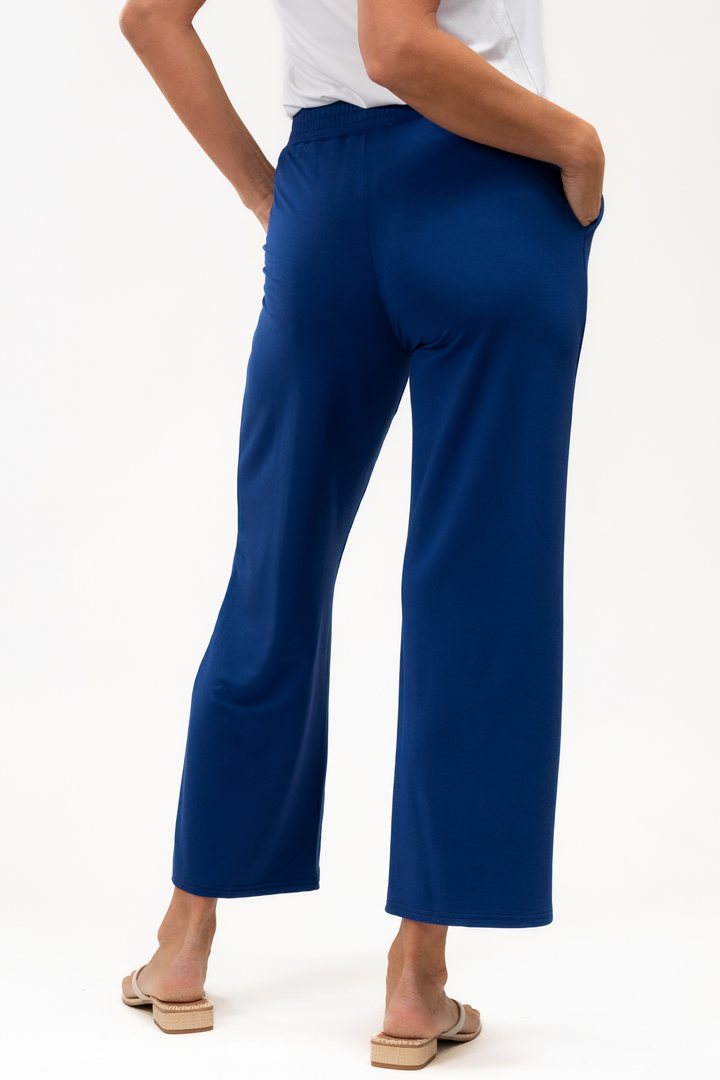 Back view of a person wearing blue ankle pants on a white background