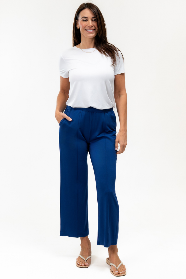 A woman wearing a white top and blue pants with flip flops on a white background
