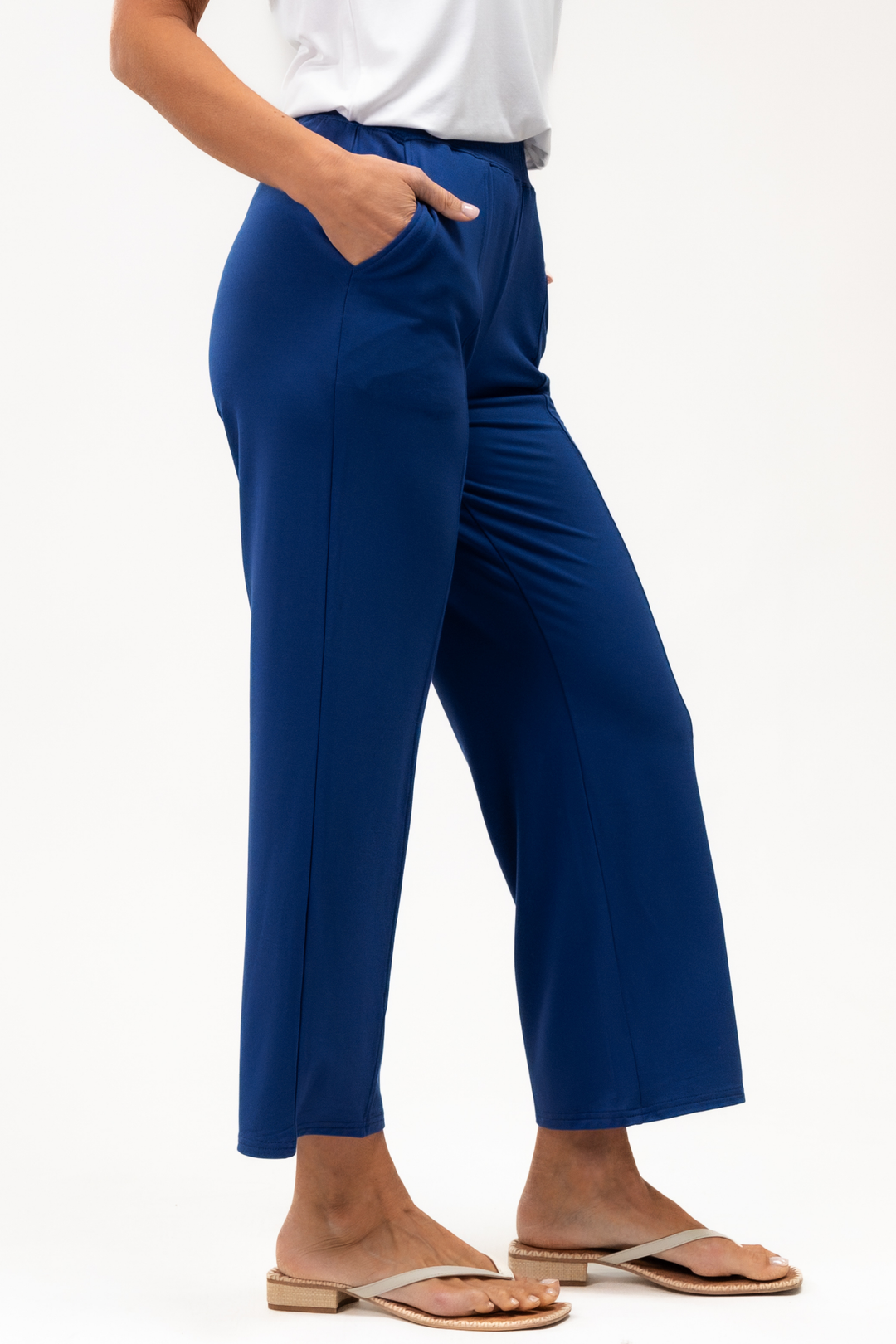 Person wearing blue ankle pants on a white background with flip flops