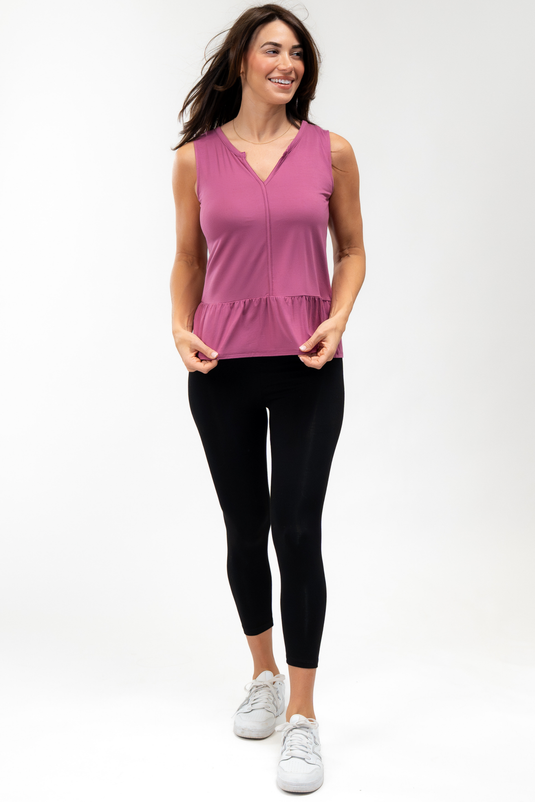 Woman wearing a pink sleeveless top with peplum hem and black bamboo leggings on a white background