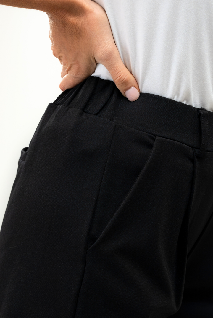 Person wearing black pants with a white shirt, focusing on the elastic waist area.