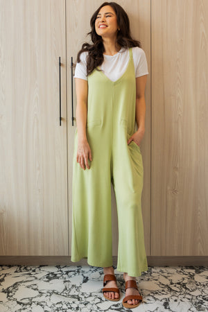 Model wearing a Citron green bamboo jumpsuit with wide legs, pockets, and adjustable thin straps. Layered underneath the jumpsuit is a white t-shirt. Model is showing the front view of the jumpsuit.