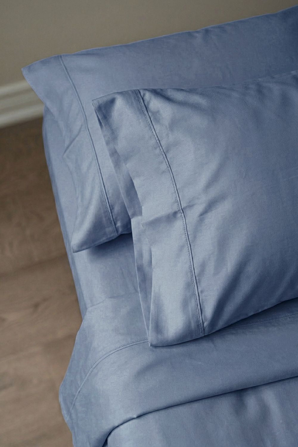 Close-up of blue bedding with a pillow on a wooden floor.
