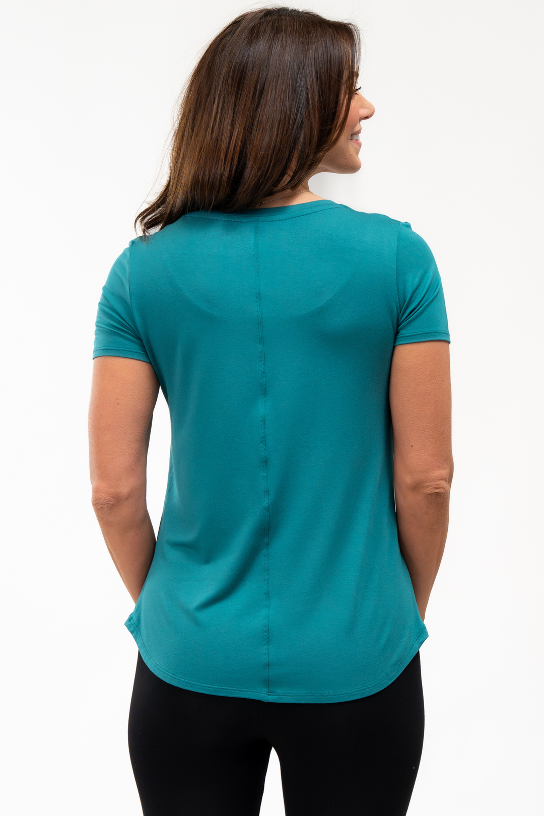 Back view of woman wearing a teal shirt on a white background showing the center seam line of the t-shirt