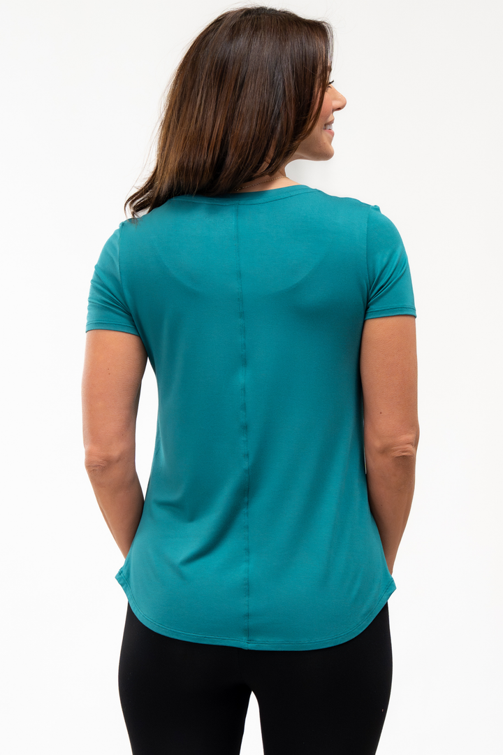 Back view of woman wearing a teal shirt on a white background showing the center seam line of the t-shirt