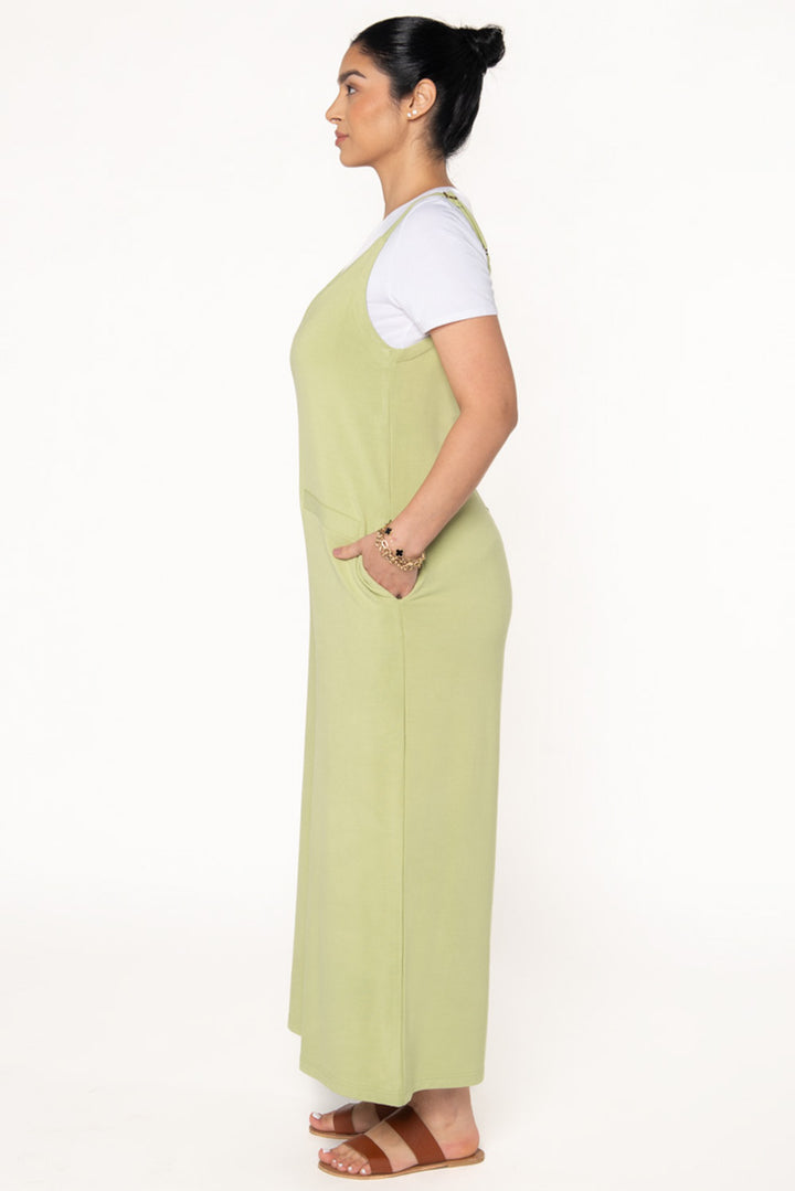 Model wearing a Citron green bamboo jumpsuit with wide legs, pockets, and adjustable thin straps. Layered underneath the jumpsuit is a white t-shirt. Model is showing the side view of the jumpsuit.