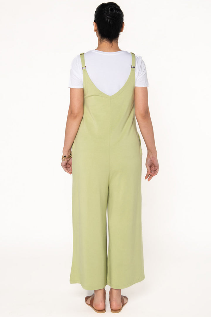 Model wearing a Citron green bamboo jumpsuit with wide legs, pockets, and adjustable thin straps. Layered underneath the jumpsuit is a white t-shirt. Model is showing the back of the jumpsuit.