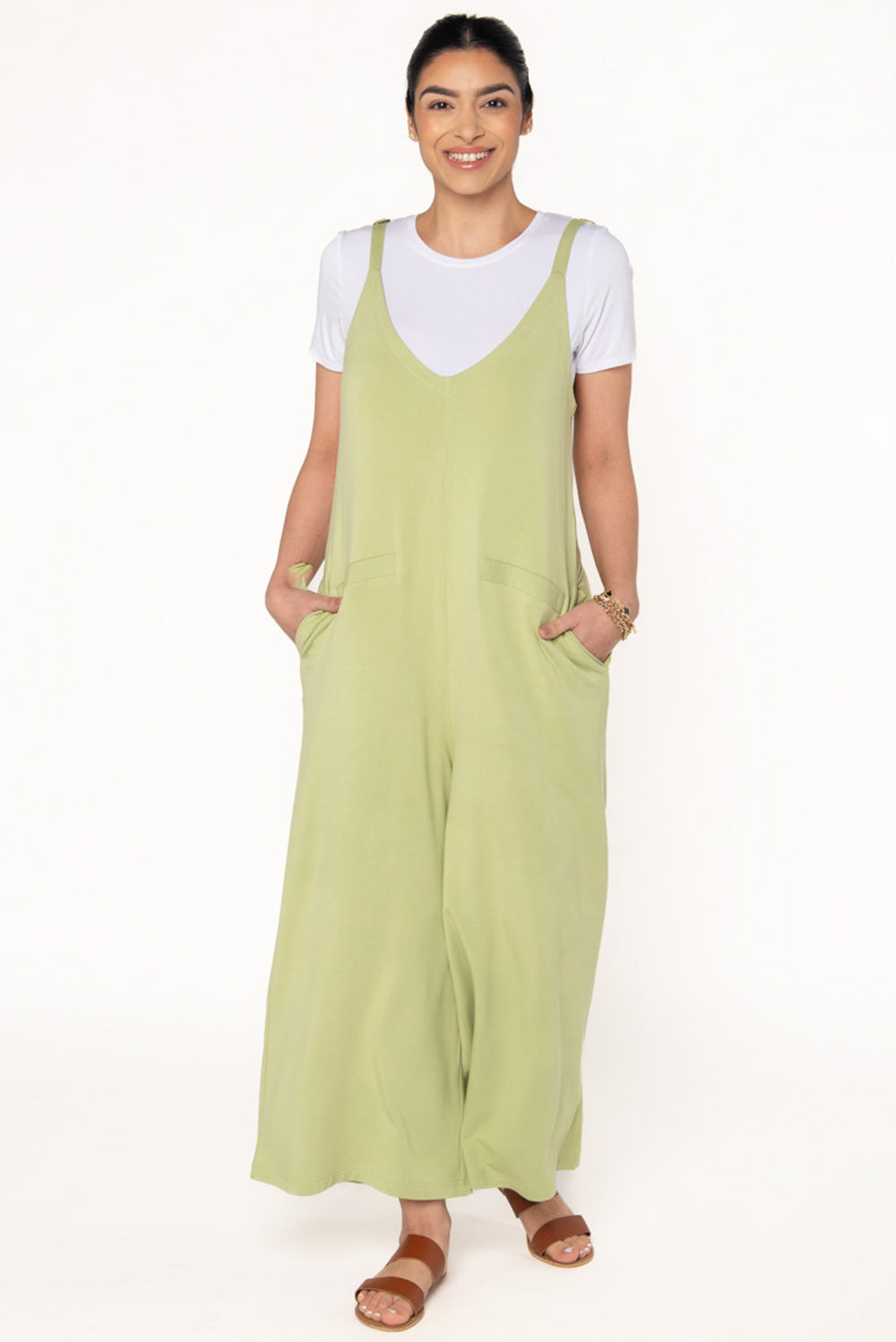 Model wearing a bamboo jumpsuit in a light green colour. The jumpsuit features wide legs, pockets, and adjustable thin straps. Layered underneath the jumpsuit is a white t-shirt. 