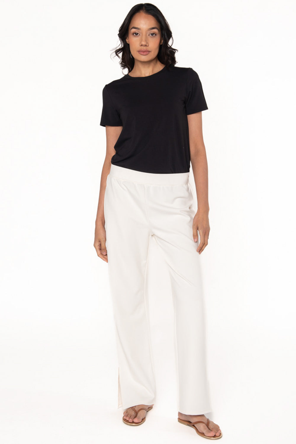 Cream coloured bamboo ponte pants worn by a model paired with a black t-shirt and brown flip flop sandals. 