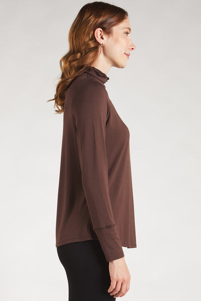  Side view of woman styling a brown long sleeve turtleneck top by Terrera.