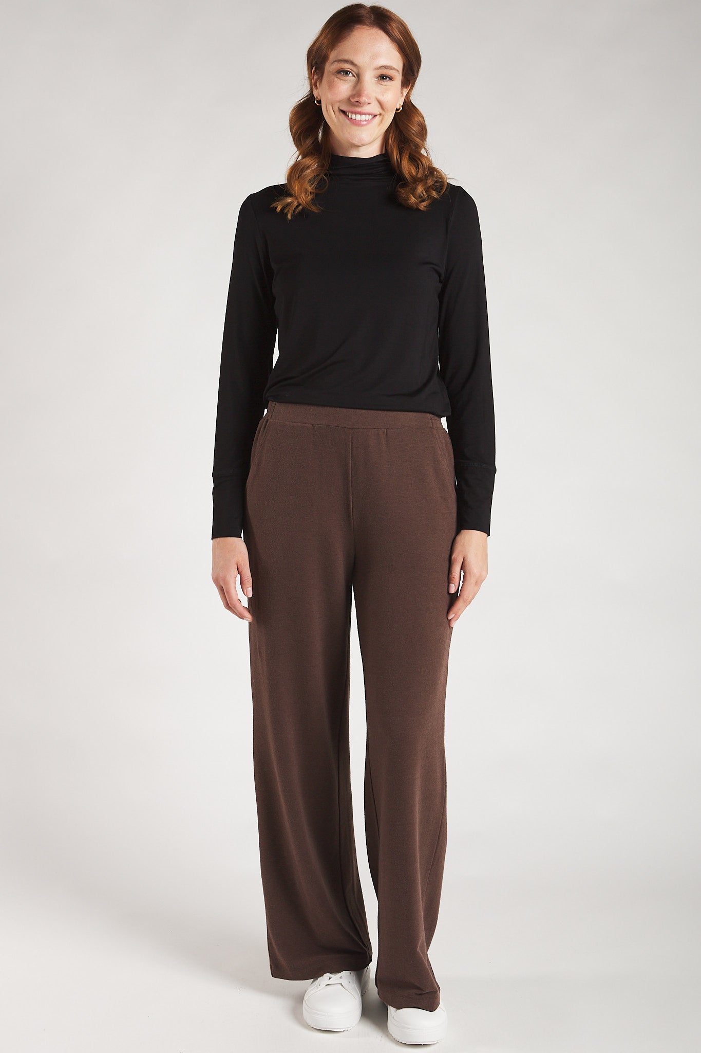 Woman styling a black long sleeve turtleneck top with brown straight leg pants from Terrera.