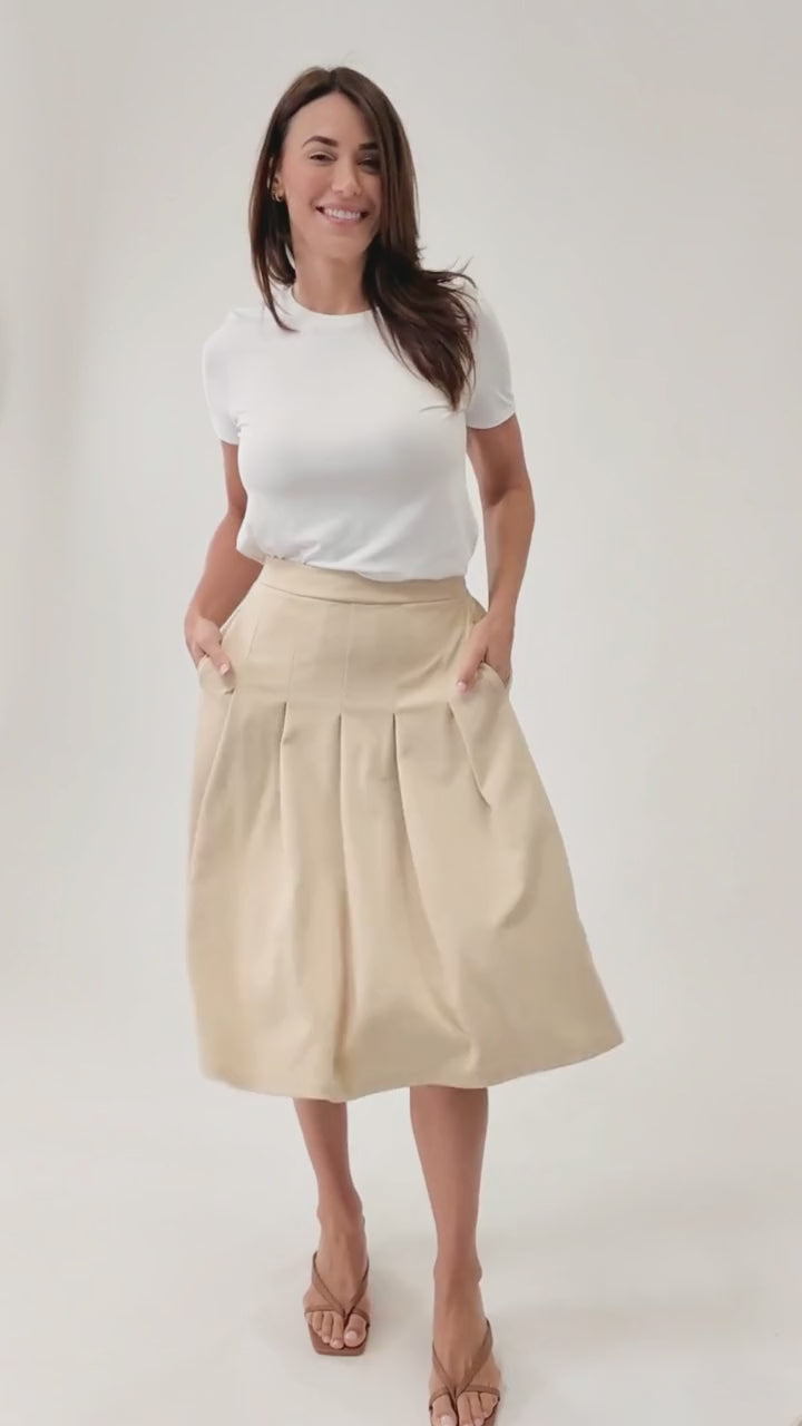 A video of a woman wearing a beige pleated skirt with a white t-shirt