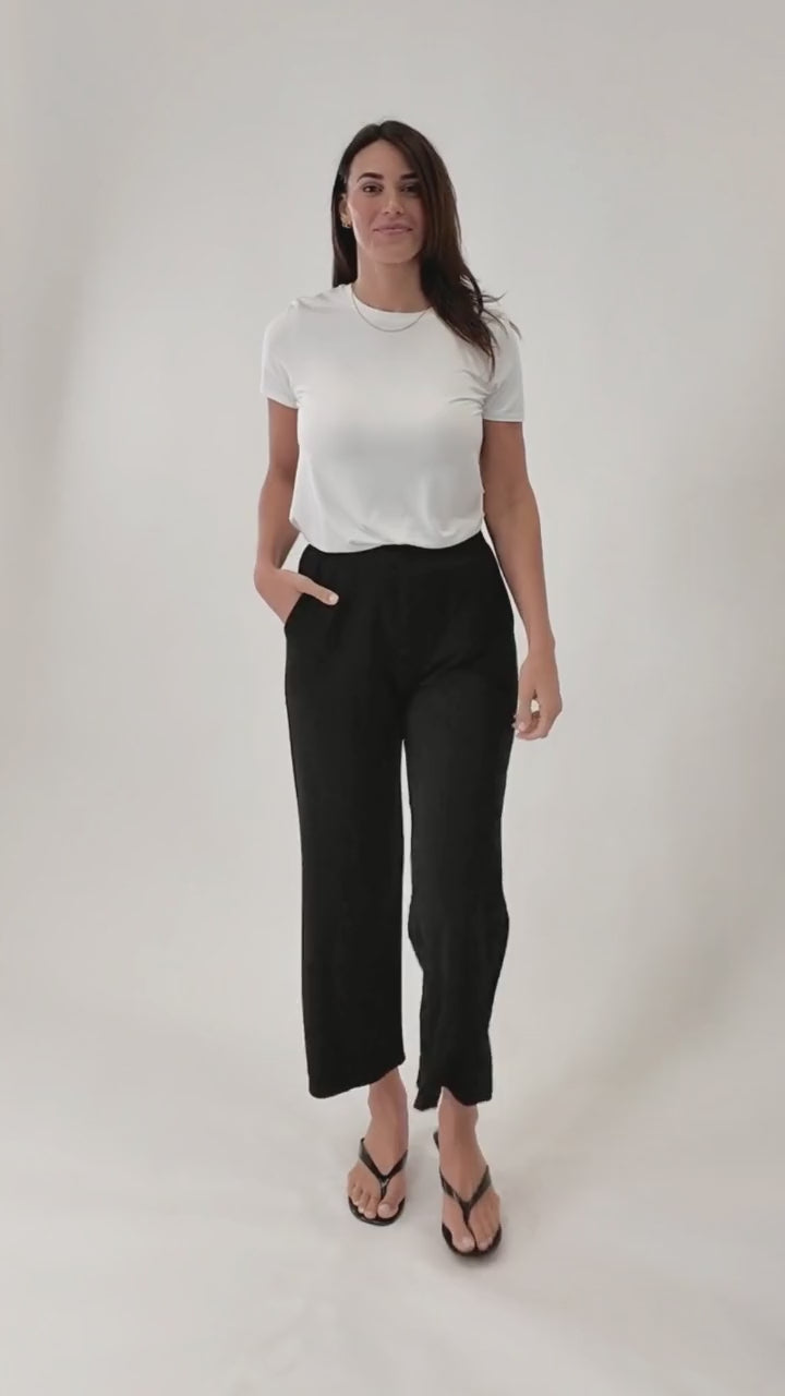 A video of a woman wearing a white top and black pants on a white background